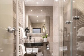 A modern bathroom with a glass shower enclosure, a marble-tiled wall, a large mirror, and a potted orchid.