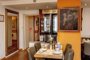 A dining area with a table set for four, a refrigerator, and a painting on the wall.