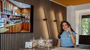 Uma área de recepção com painel de parede de madeira, uma televisão exibindo o interior de um restaurante e um balcão com potes de biscoitos.