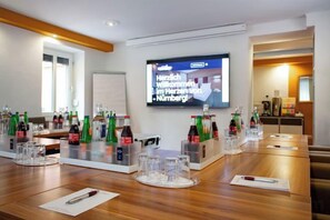 Une salle de conférence avec une longue table préparée pour une réunion, un écran de télévision et diverses bouteilles et verres.