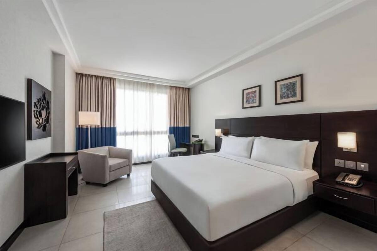 Une chambre d’hôtel avec un grand lit, un bureau, une chaise, une télévision et une fenêtre avec des rideaux.