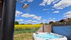 A hot tub in a garden with a showerhead above it, surrounded by a field of yellow flowers and a clear blue sky. - Beach house on the Rhön beach with whirlpool (Wartmannsroth)