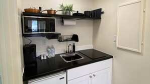 A compact kitchen with a microwave, sink, and white cabinets.