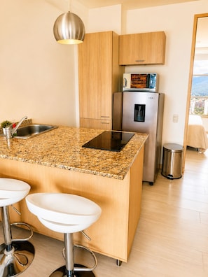 A modern kitchen with a granite countertop, stainless steel appliances, and wooden cabinets. - Lovely one bedroom condo in Laureles (Medellín)
