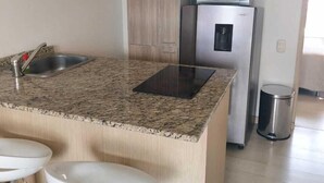 A modern kitchen with a granite countertop, stainless steel appliances, and wooden cabinets. - Lovely one bedroom condo in Laureles (Medellín)