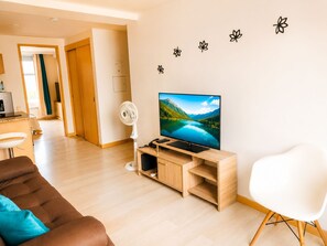 A modern living room with a flat-screen TV, a white fan, a brown sofa, and a white chair.