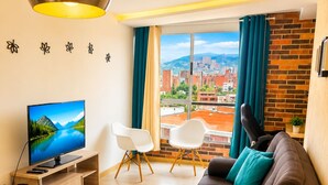 A modern living room with a television, sofa, chairs, and a view of a cityscape through large windows.