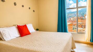 Habitación de hotel con cama, ventana con vista a la ciudad y decoración floral en la pared.