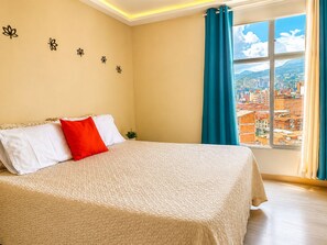 Habitación de hotel con cama, ventana con vista a la ciudad y decoración floral en la pared.
