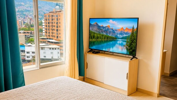 A hotel room with a bed, a television on a wooden cabinet, and a window with curtains.