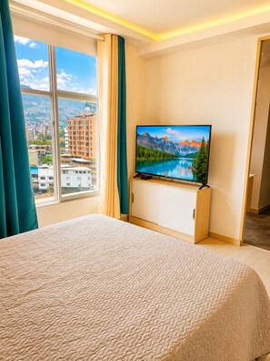 Una camera d'albergo con un letto, una televisione su un mobile in legno e una finestra con tende.