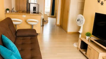 A modern living room with a brown sofa, a TV on a wooden stand, and a kitchen area in the background.