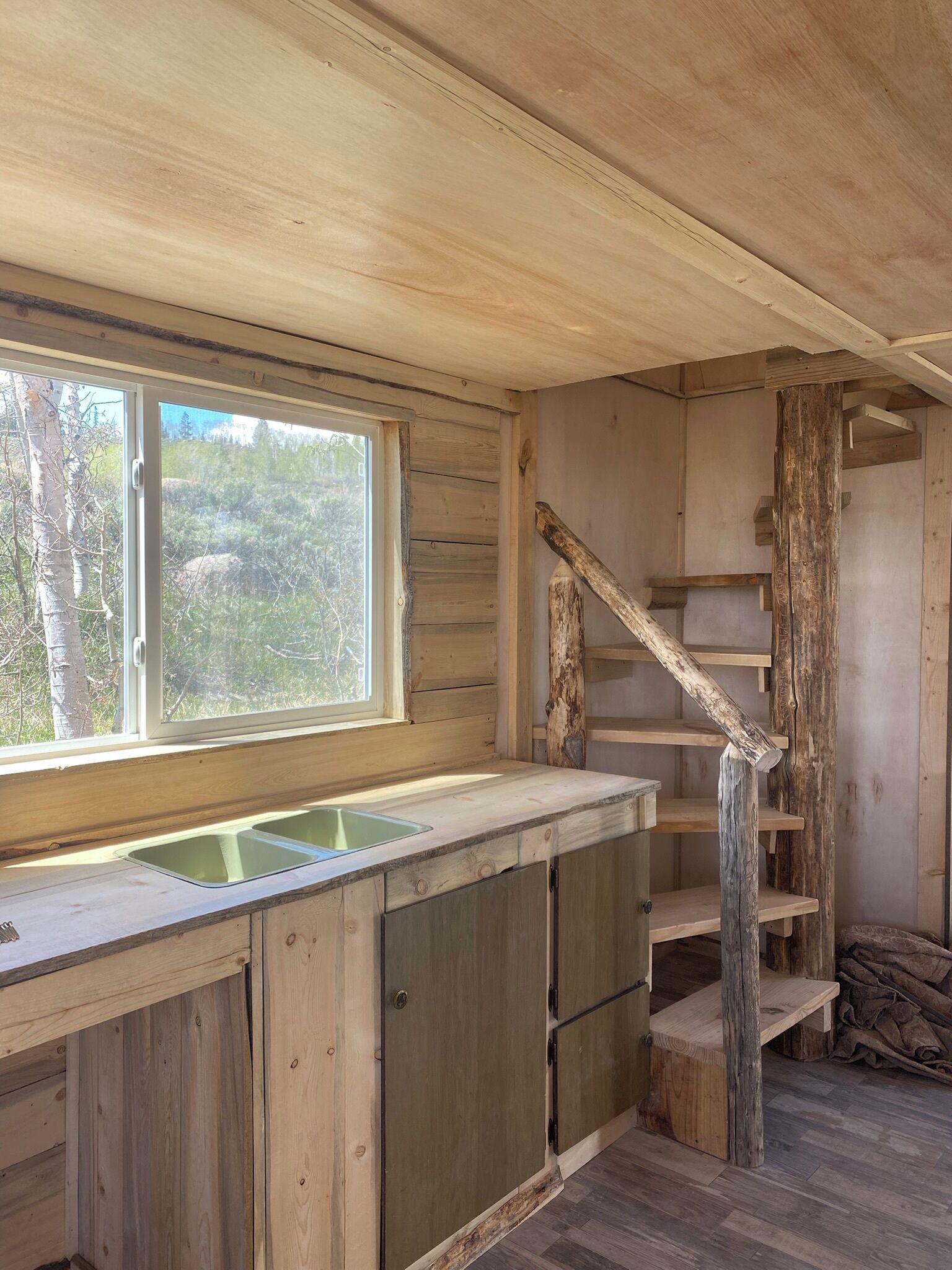 A rustic kitchen with a large window, wooden cabinets, and a wooden staircase.