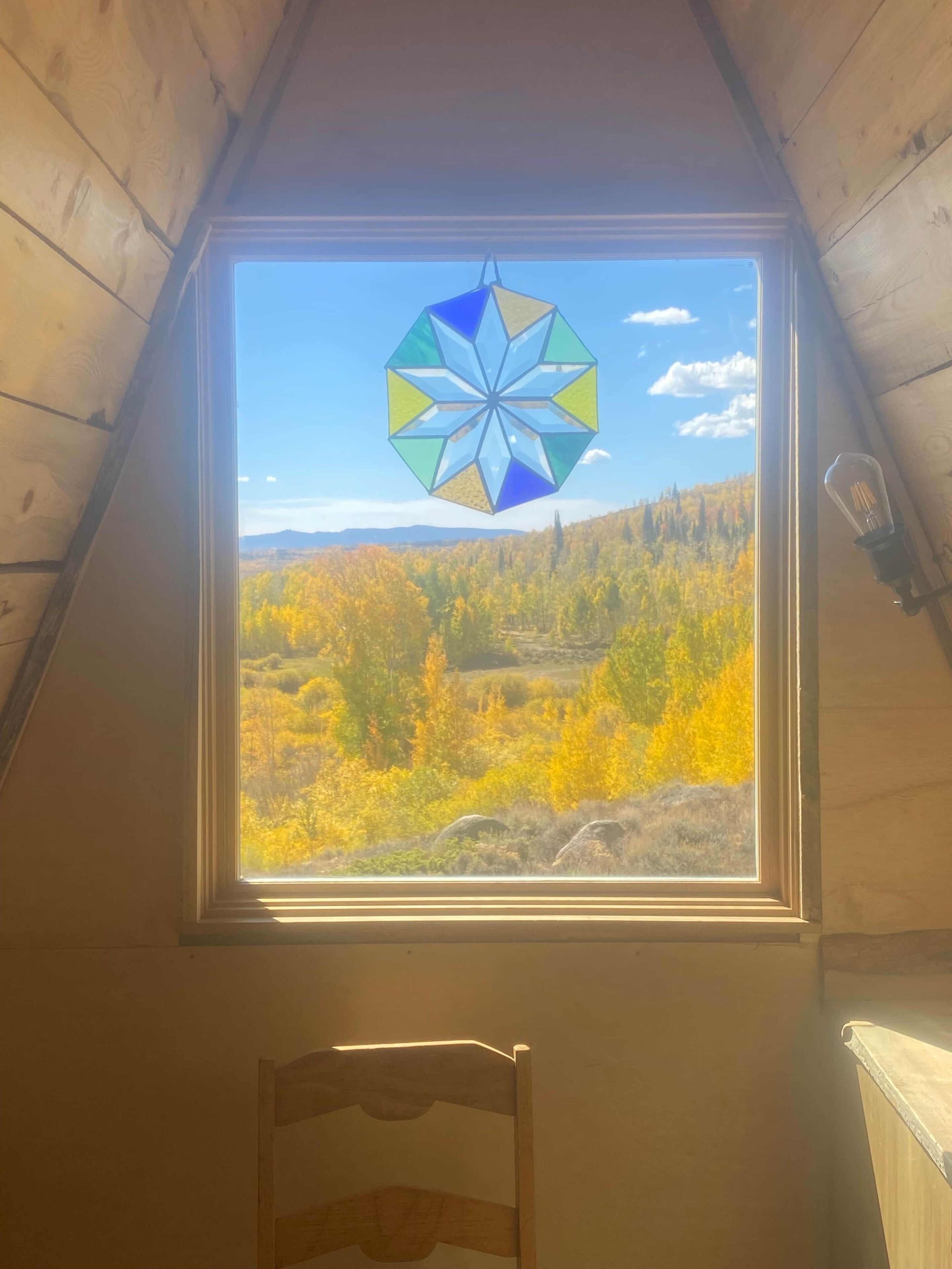 A room with a sloped ceiling, a window with a star-shaped stained glass, and a view of autumn foliage.