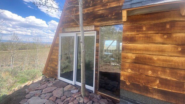 A wooden cabin with a stone foundation, large sliding glass doors, and a view of the surrounding landscape. - Pronghorn Point Cabin@22 West Cabins 18miles from Walden 80 miles from Steamboat (Walden)
