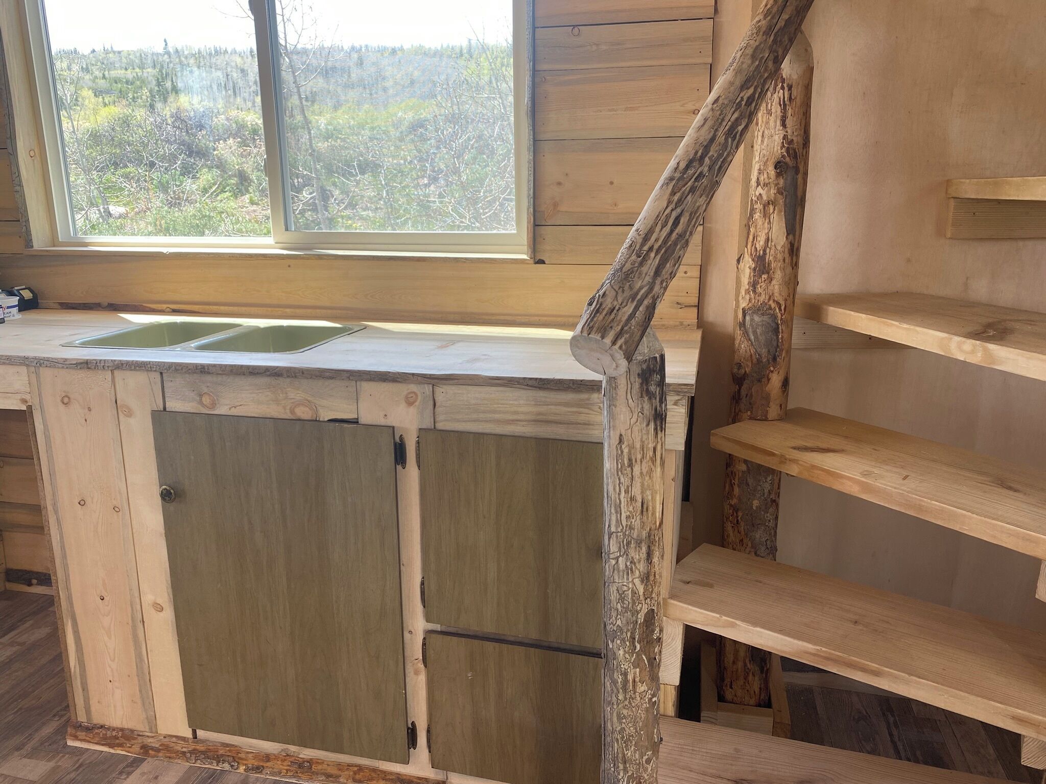 Een landelijke keuken met een houten aanrecht, een spoelbak en uitzicht op een bos door een raam.