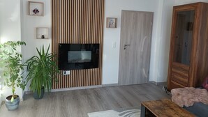 A modern living room with a wooden slat wall, a flat-screen TV, a wooden door, and a large potted plant.