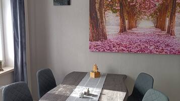 Ein Essbereich mit einem Holztisch, gepolsterten Stühlen, einer an der Wand befestigten Uhr und einem großen Blumenbild.