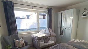 A bedroom with a bed, a chair, a small table, a window with curtains, and a wardrobe.