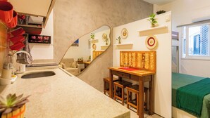 A compact room with a kitchenette, a small dining table, a bed with a green blanket, and a mirror reflecting the room. - SUH Copacabana 79 New Beach (Rio de Janeiro)