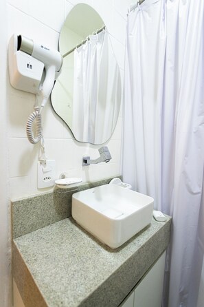 Un baño con lavamanos blanco, secador de pelo, espejo y cortina de ducha.