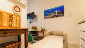 A compact room with a bed, a small desk, a television, and a painting of a cityscape. - SUH Copacabana 79 New Beach (Rio de Janeiro)