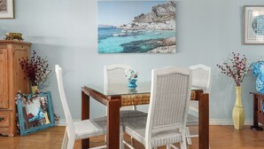 Un comedor con una mesa de vidrio, sillas de mimbre y un cuadro de temática costera en la pared.