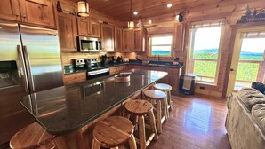 A kitchen with wooden cabinets, stainless steel appliances, a large island with stools, and a view of the outdoors through a window. - New Amazing View Cabin, 5 miles to Dollywood, 12 miles to Smokies, Sleeps 11 (Sevierville)