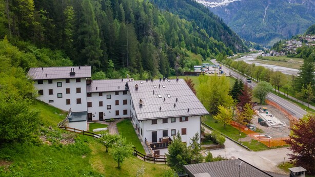 Uma área residencial com dois edifícios brancos, uma estrada e montanhas ao fundo.