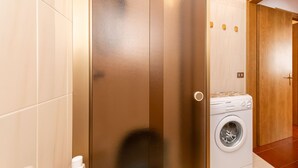 Uma casa de banho moderna com um espelho grande, uma máquina de lavar roupa e uma porta de madeira.