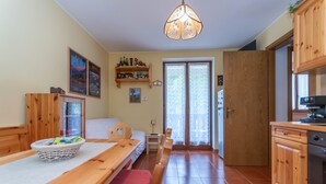 Um quarto aconchegante com uma mesa de jantar de madeira, bancos, uma cama, uma pequena mesa com um cesto, um armário de madeira e uma cozinha com fogão.
