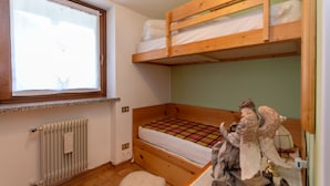 Quarto pequeno com cama de solteiro, janela, radiador e beliche de madeira.