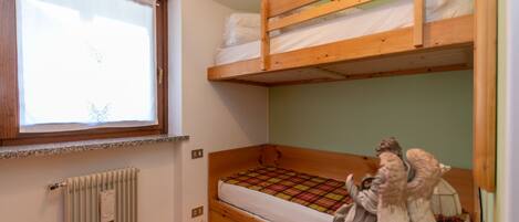 Habitación pequeña con cama individual, ventana, radiador y litera de madera.