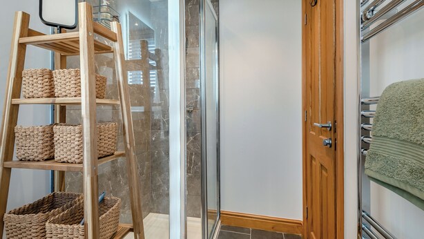 Een badkamer met een houten laddenplank met manden, een glazen douchecabine en een handdoekhouder met een groene handdoek.