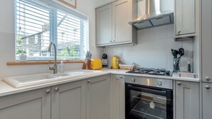 Een moderne keuken met een gasfornuis, oven en een raam met zonwering.