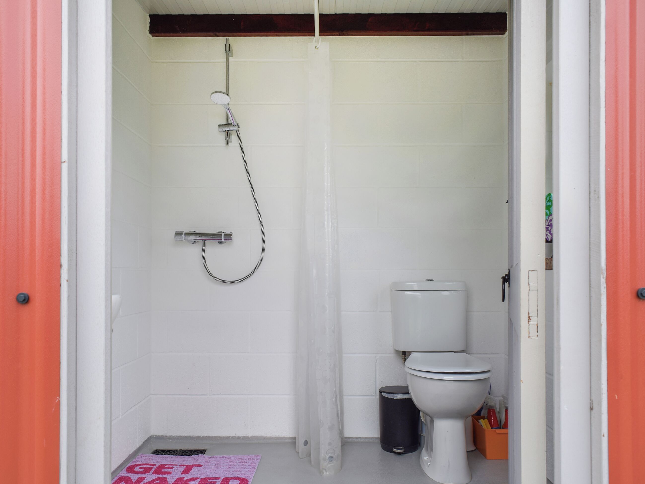 A small, compact bathroom with a shower, toilet, and trash bin.