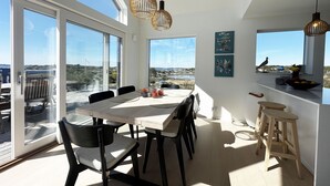 A modern dining area with a large table, chairs, pendant lights, and artwork on the walls.