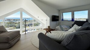 A modern living room with a large window, a flat-screen TV, and a cozy seating area.