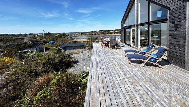 A modern house with a deck, lounge chairs, and a view of the landscape.