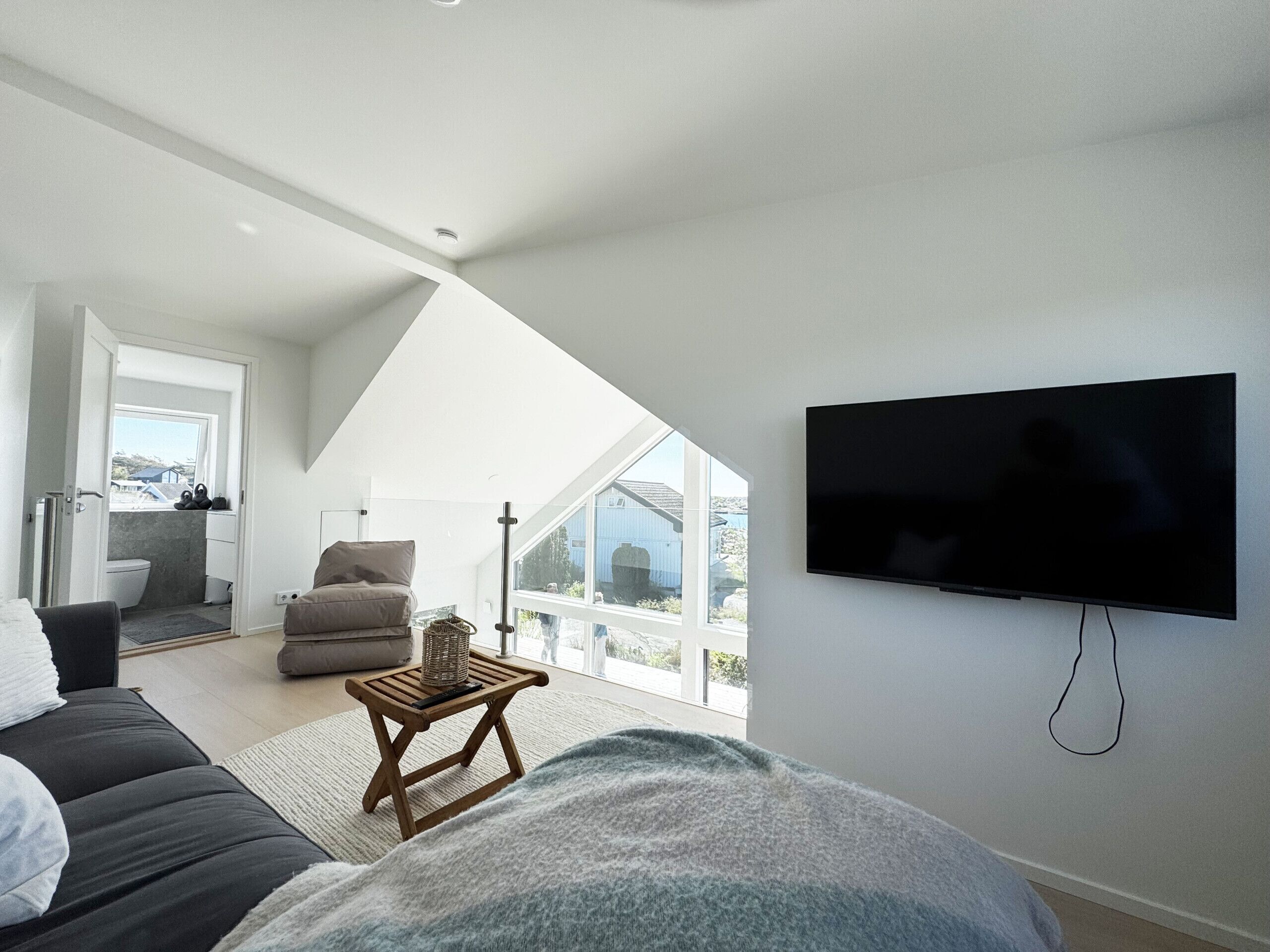 A modern living room with a large TV, a sofa, a chair, and a view of the outdoors.