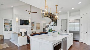 Una cocina amplia con una isla grande, armarios blancos y electrodomésticos de acero inoxidable.