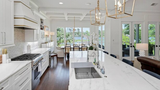 Una cocina moderna con una isla grande, armarios blancos y vistas al exterior.