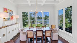 Un comedor con una mesa grande, muebles blancos y vista a un lago.