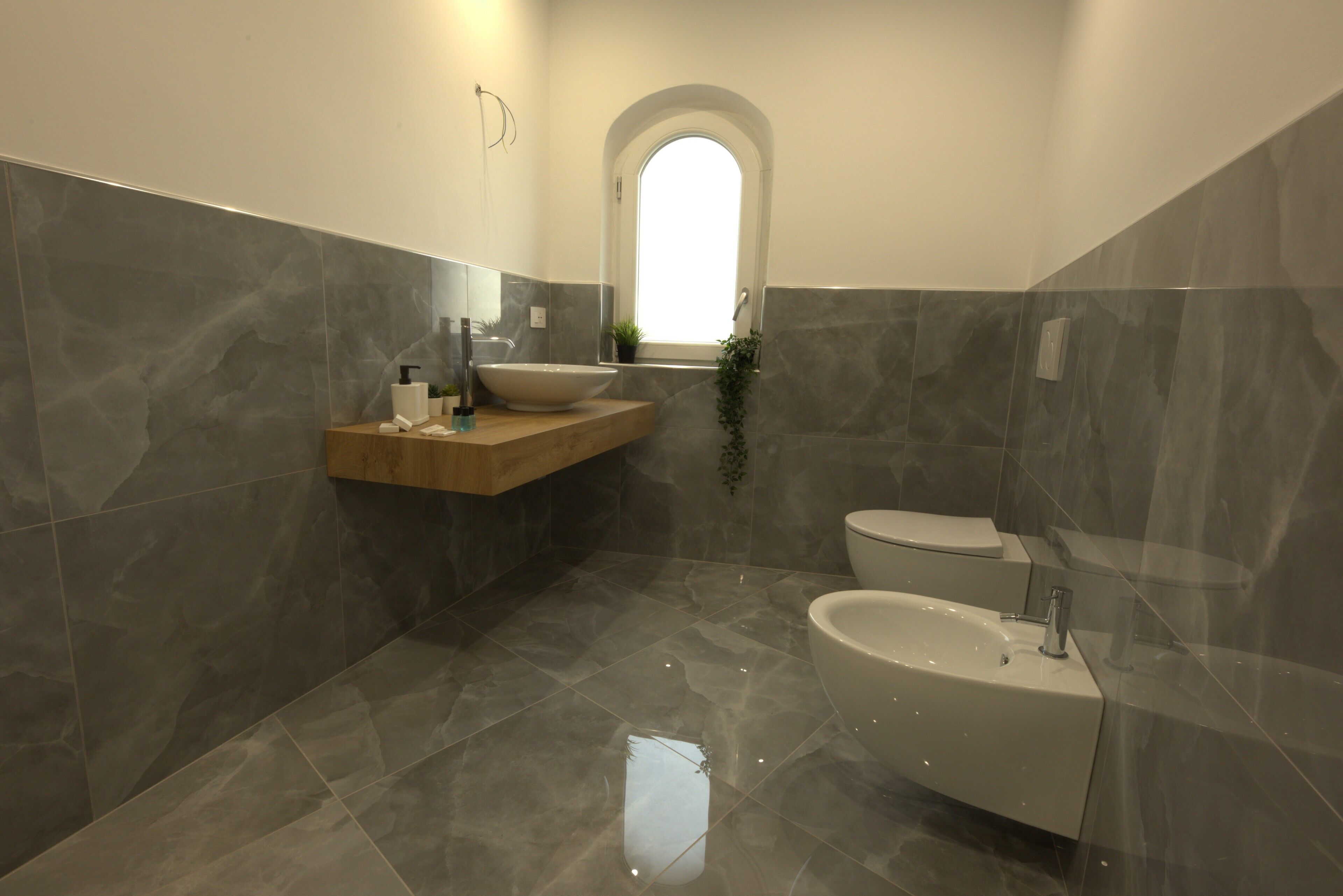 Une salle de bain moderne avec une baignoire sur pieds, un meuble-lavabo doté d’un grand miroir et une fenêtre à arc.