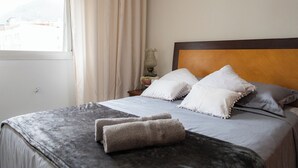 Una cama bien hecha con una colcha gris, dos almohadas blancas y una toalla gris.