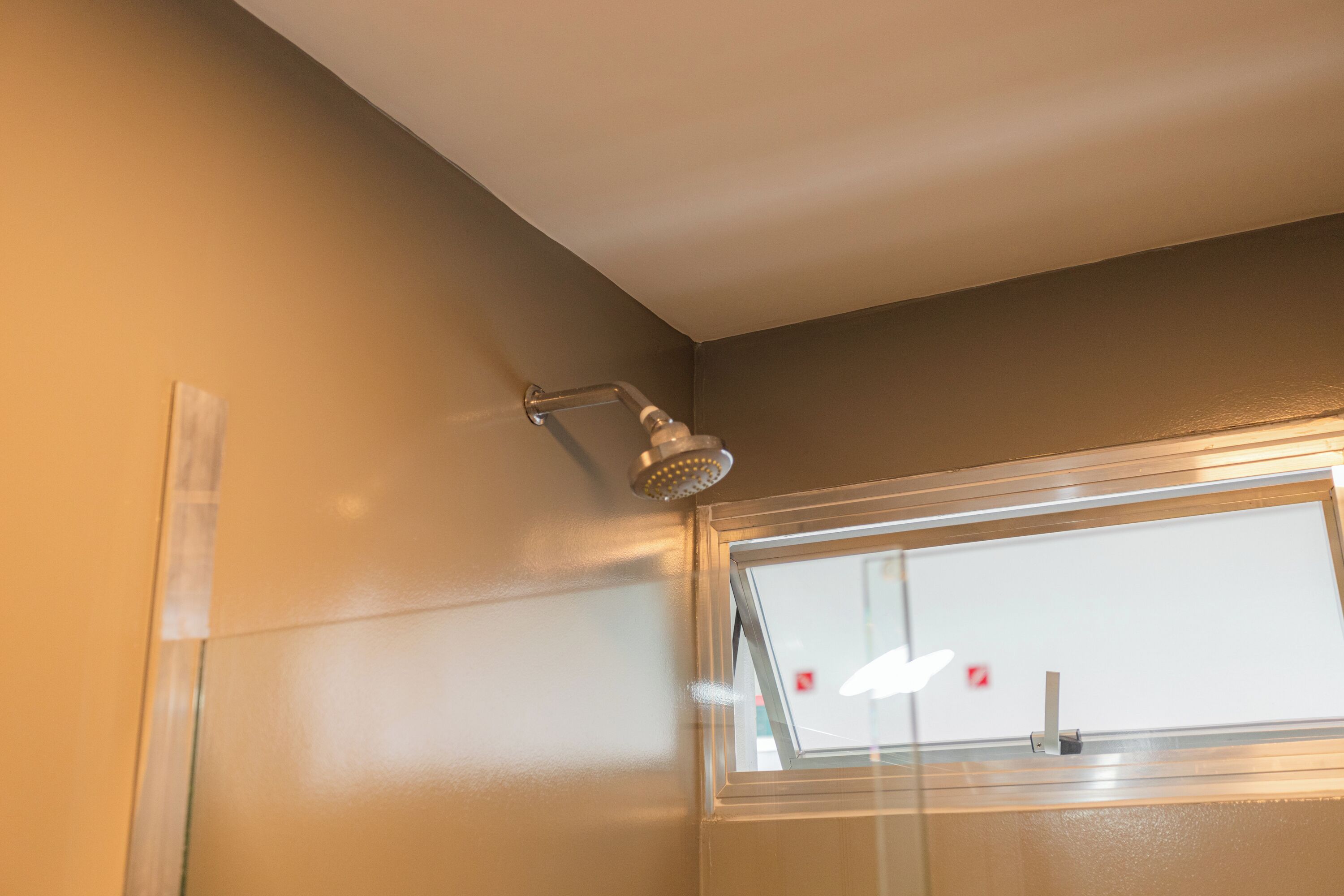 Eine Dusche mit einer Handbrause an der Wand, ein Fenster mit Blick nach draußen und eine Tür mit Griff.