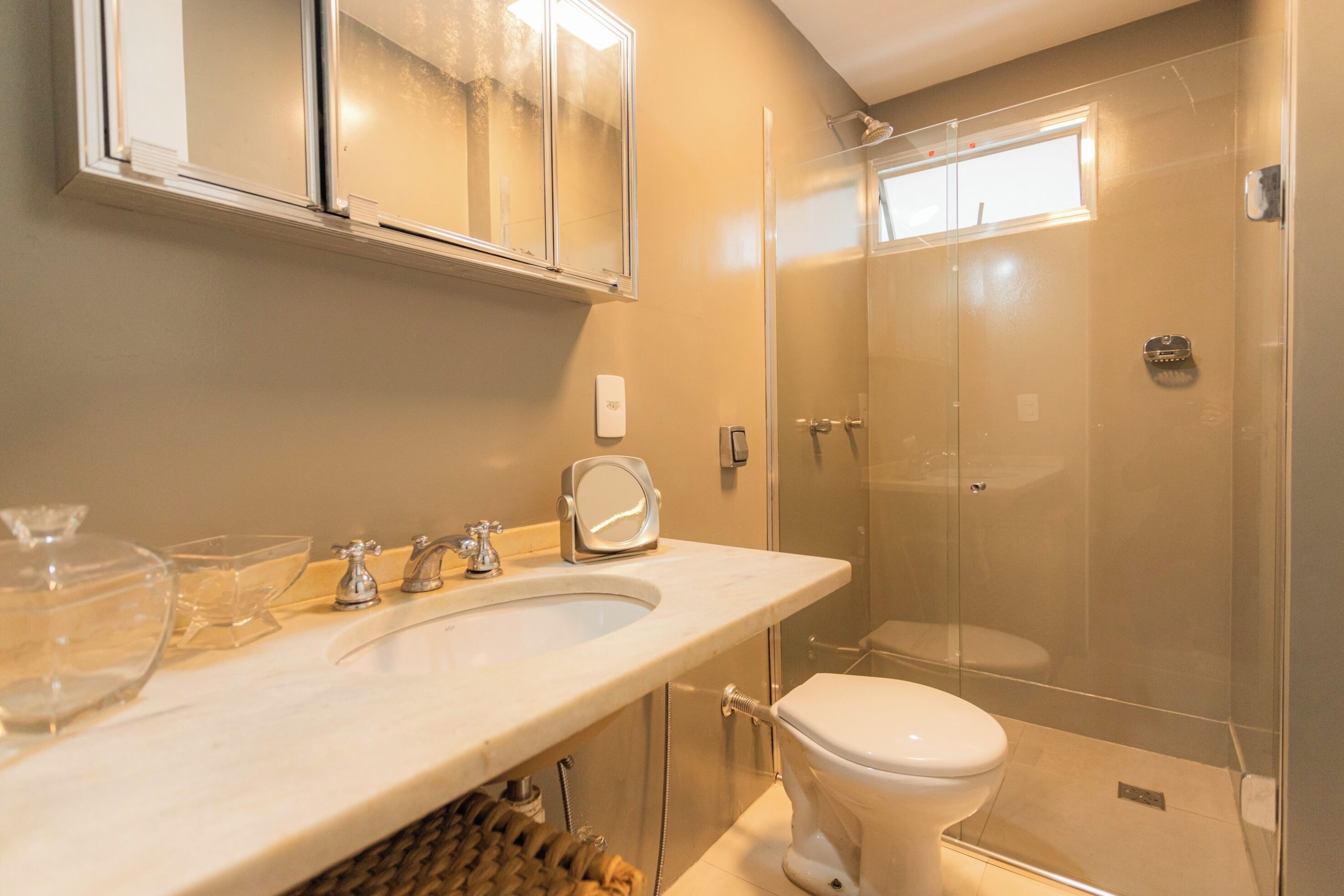 A modern bathroom with a glass-enclosed shower, a white sink with a mirror, and a toilet.