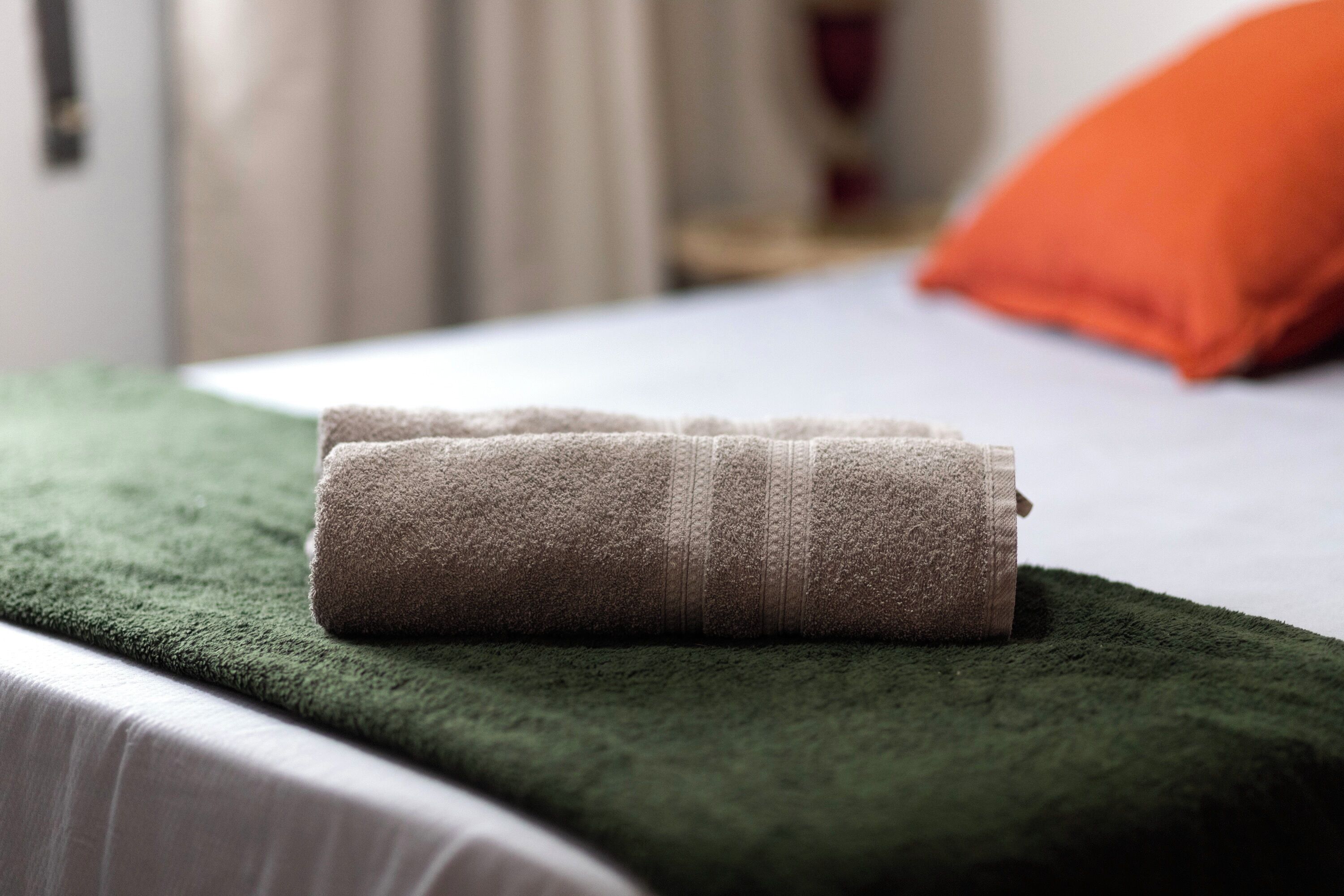 Une serviette soigneusement pliée, posée sur un couvre-lit vert dans une chambre d’hôtel.