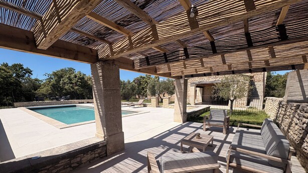 Un patio al aire libre con piscina, paredes de piedra y mobiliario de madera.