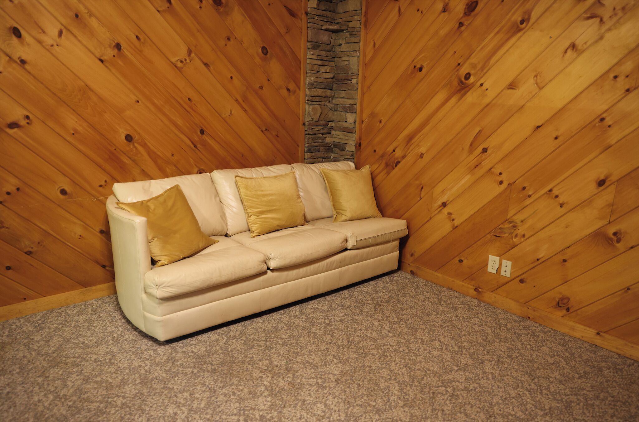 A beige sofa with four cushions against a wooden wall with a stone accent.